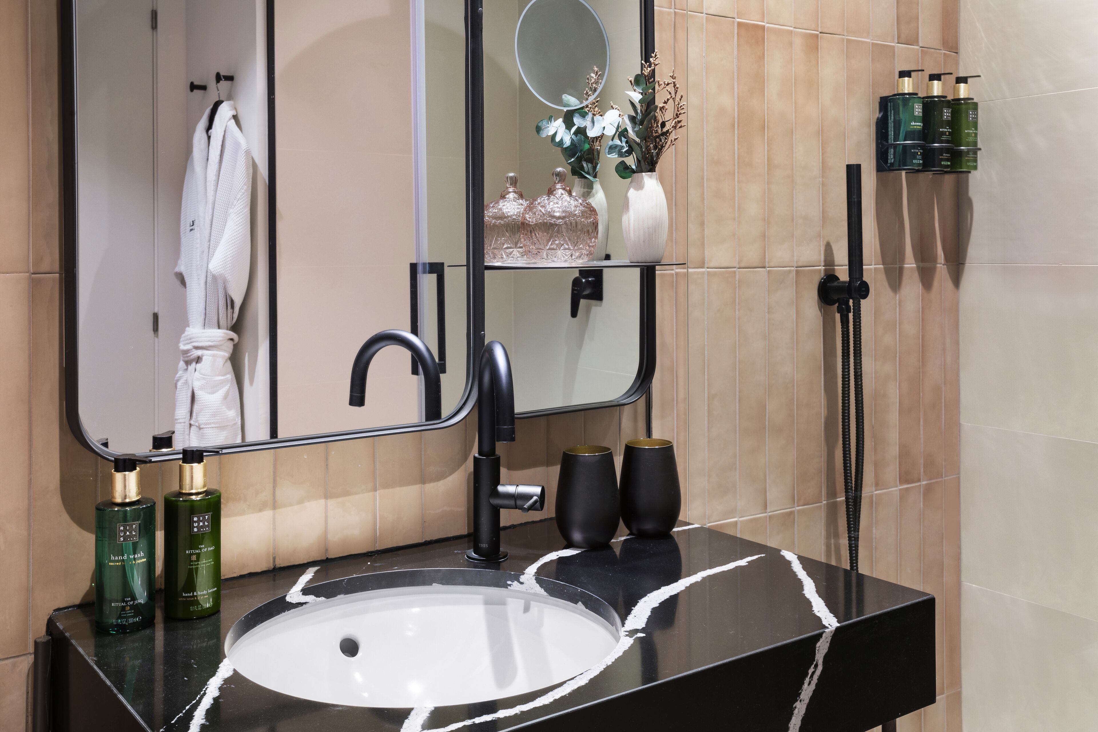 A bathroom with a black sink, a mirror, and a handheld showerhead. There are bottles of hand wash on the counter.