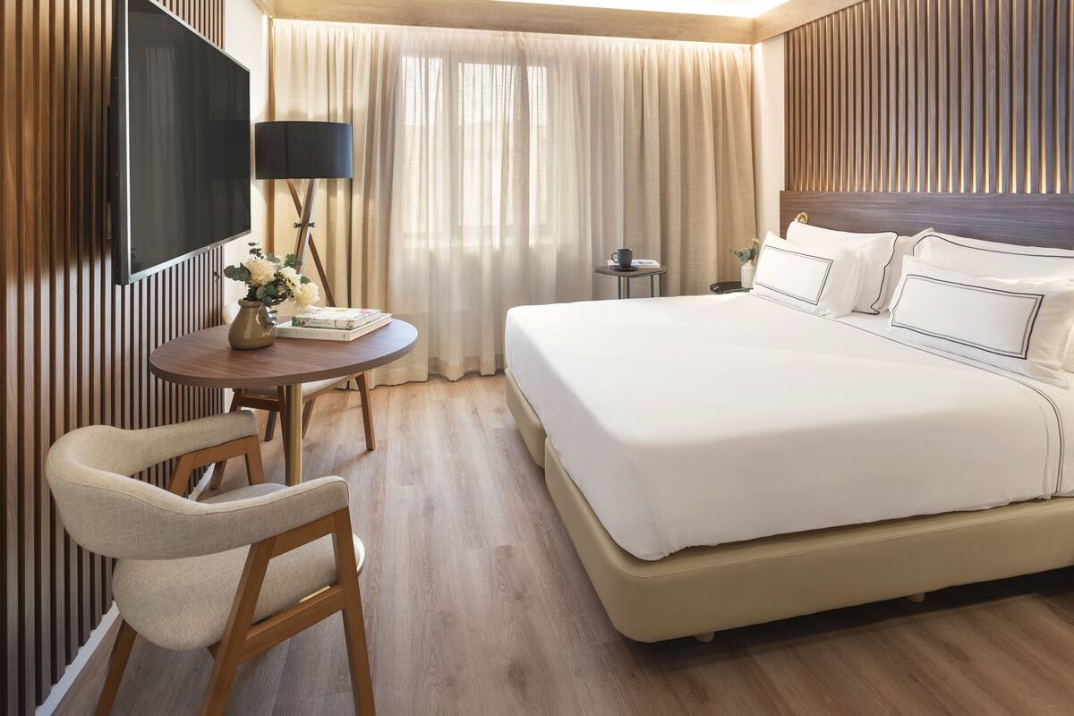 Habitación de hotel con una cama grande, televisión, escritorio con silla y ventana con cortinas.