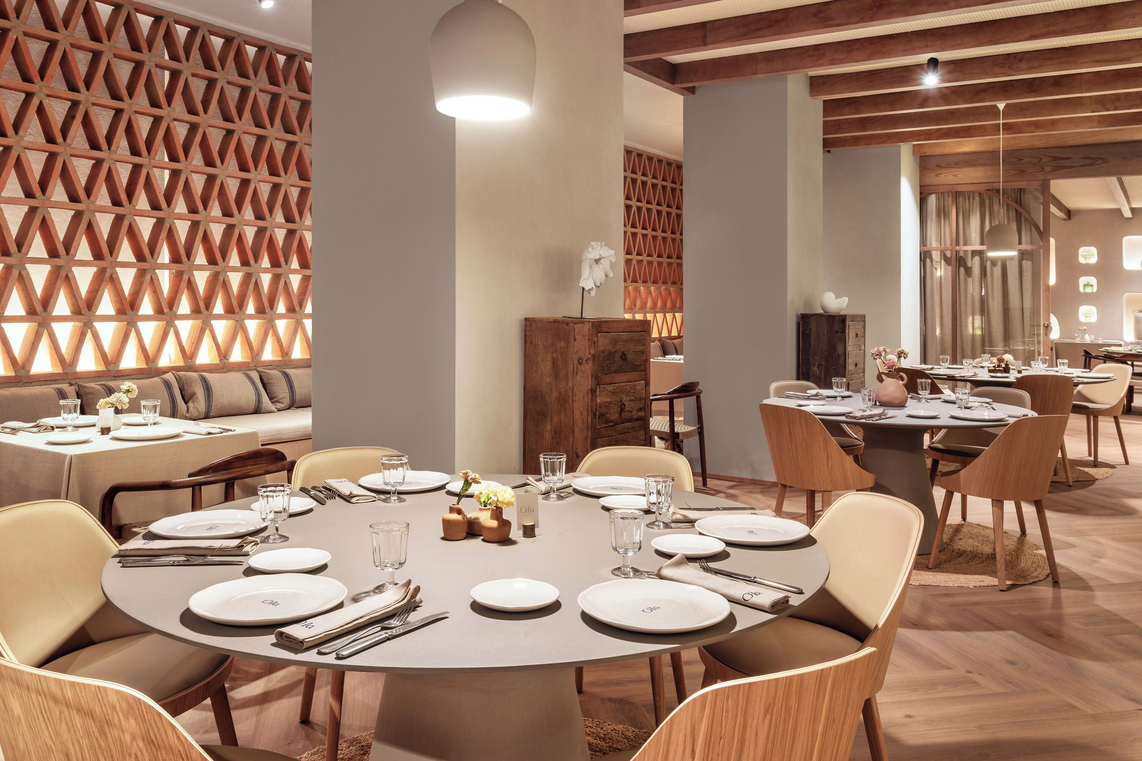 A dining area with round tables set for four, wooden chairs, and a decorative wall with a geometric pattern.