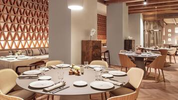 A dining area with round tables set for four, wooden chairs, and a decorative wall with a geometric pattern.