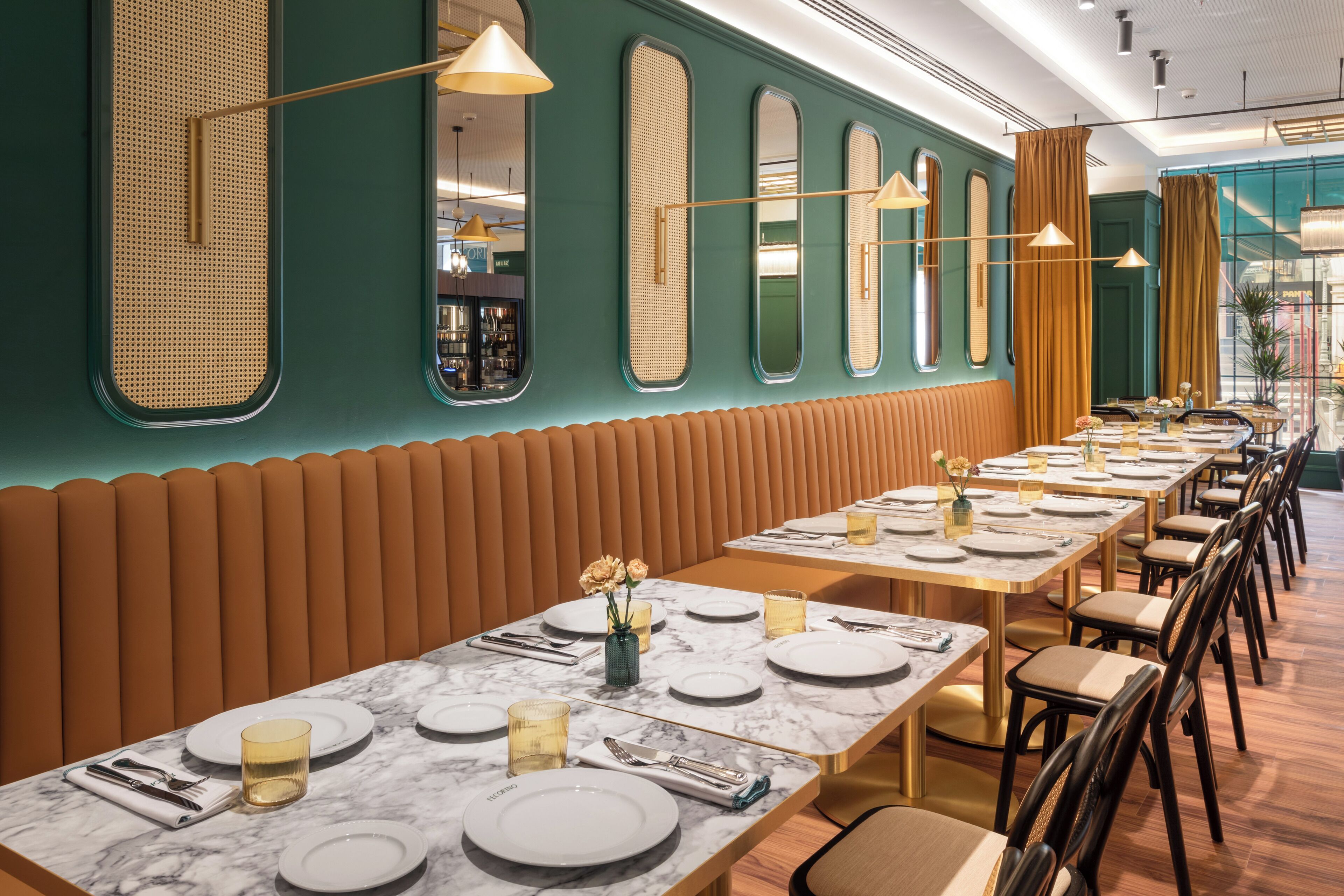 A restaurant with long tables set for dining, featuring a green wall with mirrors and a wooden bench along one side.