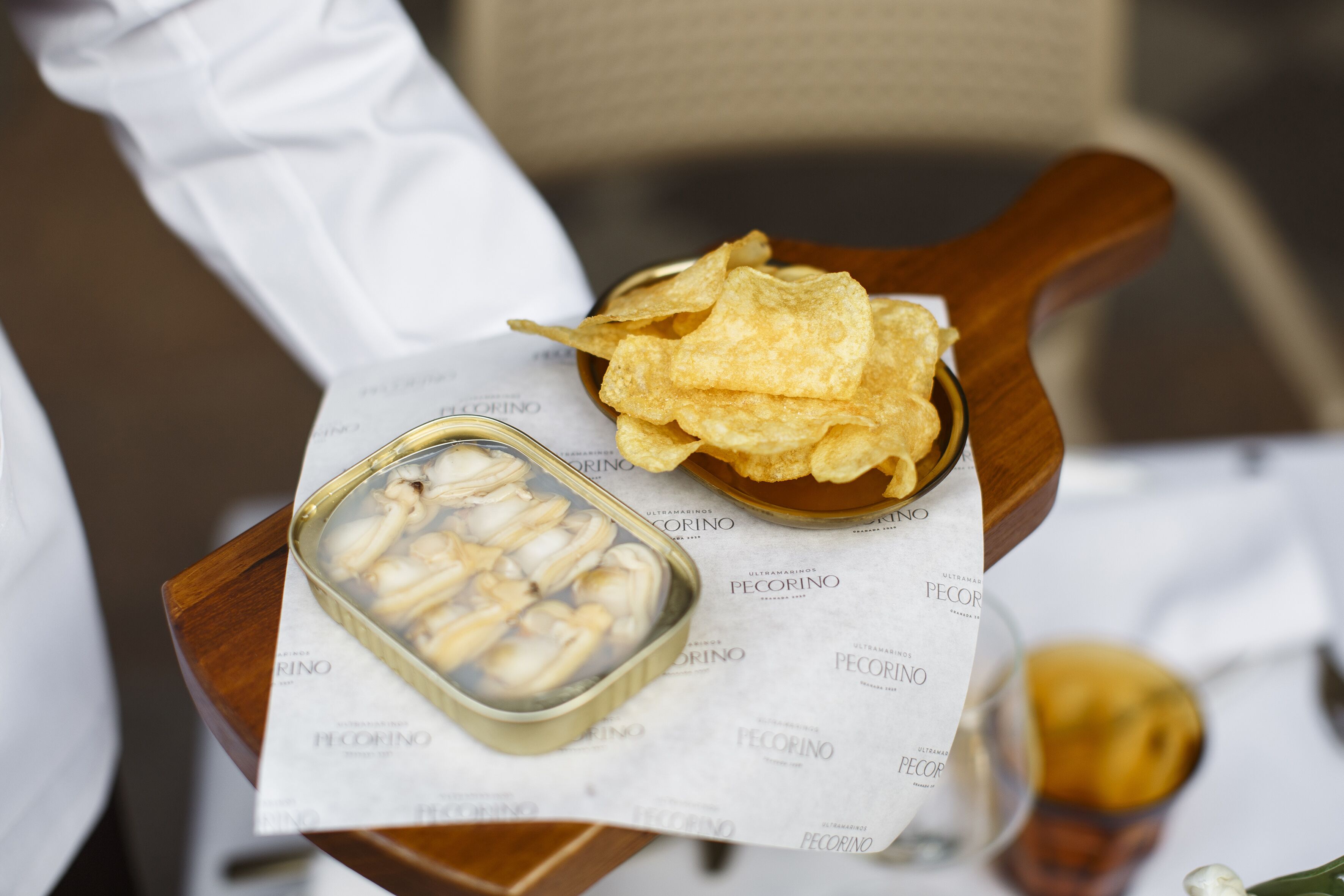 A wooden table with a bowl of corn on the cob, a plate of chips, and a small container of pickled vegetables.