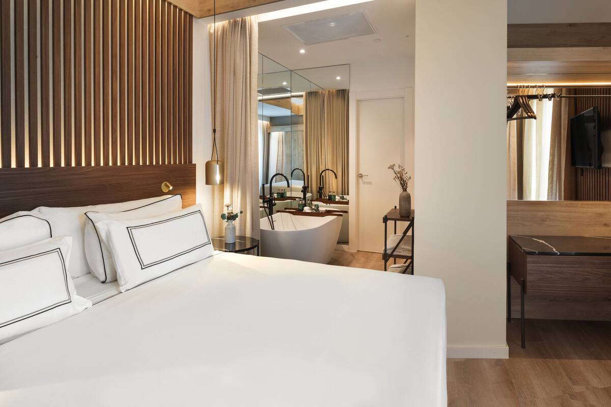 Habitación de hotel moderna con una cama grande, un baño con bañera y un panel de pared de madera.