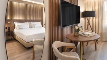 Una habitación de hotel moderna con una cama grande, un televisor de pantalla plana, una mesa redonda con sillas y una lámpara de pie.
