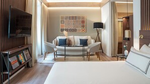 A modern hotel room with a bed, a sofa, a TV, and a coffee table. - Melia Granada Hotel (Granada)