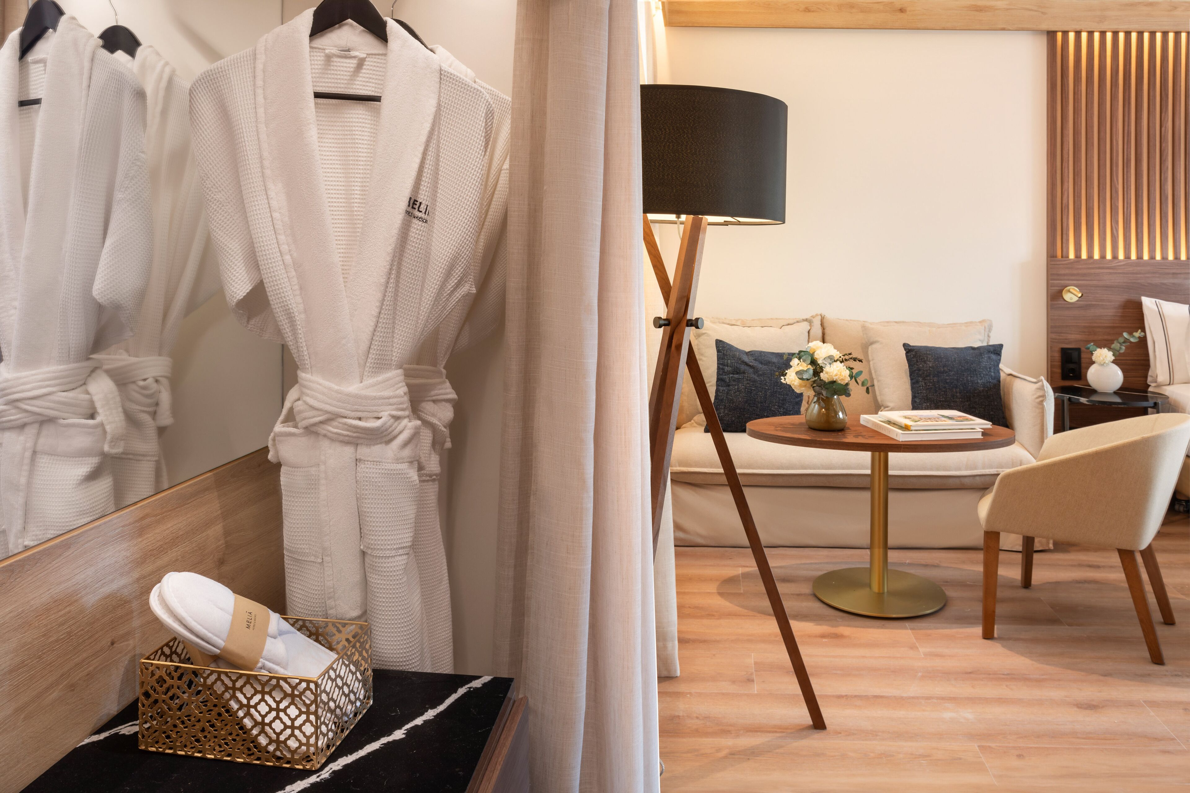 A hotel room with a wooden floor, a sofa, a chair, a lamp, and a mirror.