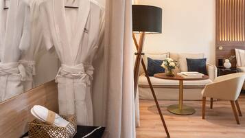 A hotel room with a wooden floor, a sofa, a chair, a lamp, and a mirror.