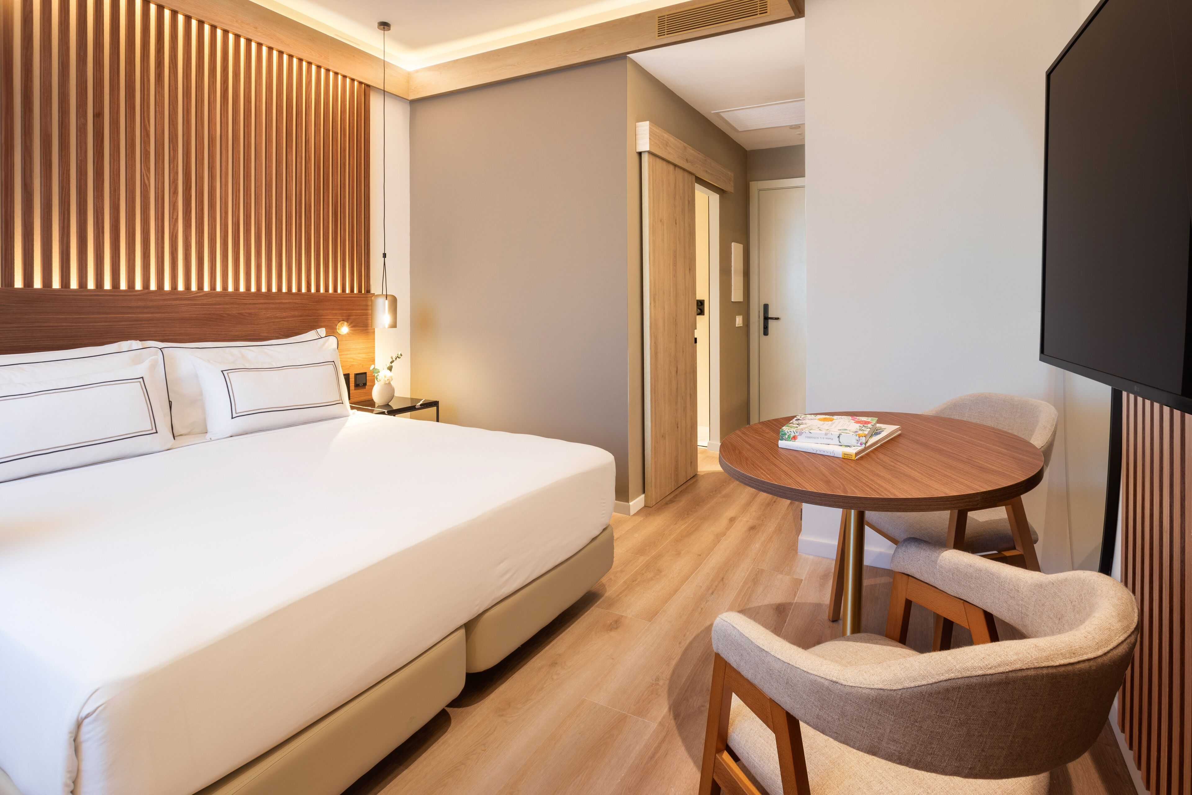 A hotel room with a large bed, a wooden headboard, a round dining table with chairs, and a television.