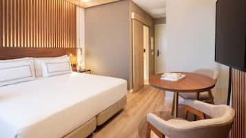 A hotel room with a large bed, a wooden headboard, a round dining table with chairs, and a television.
