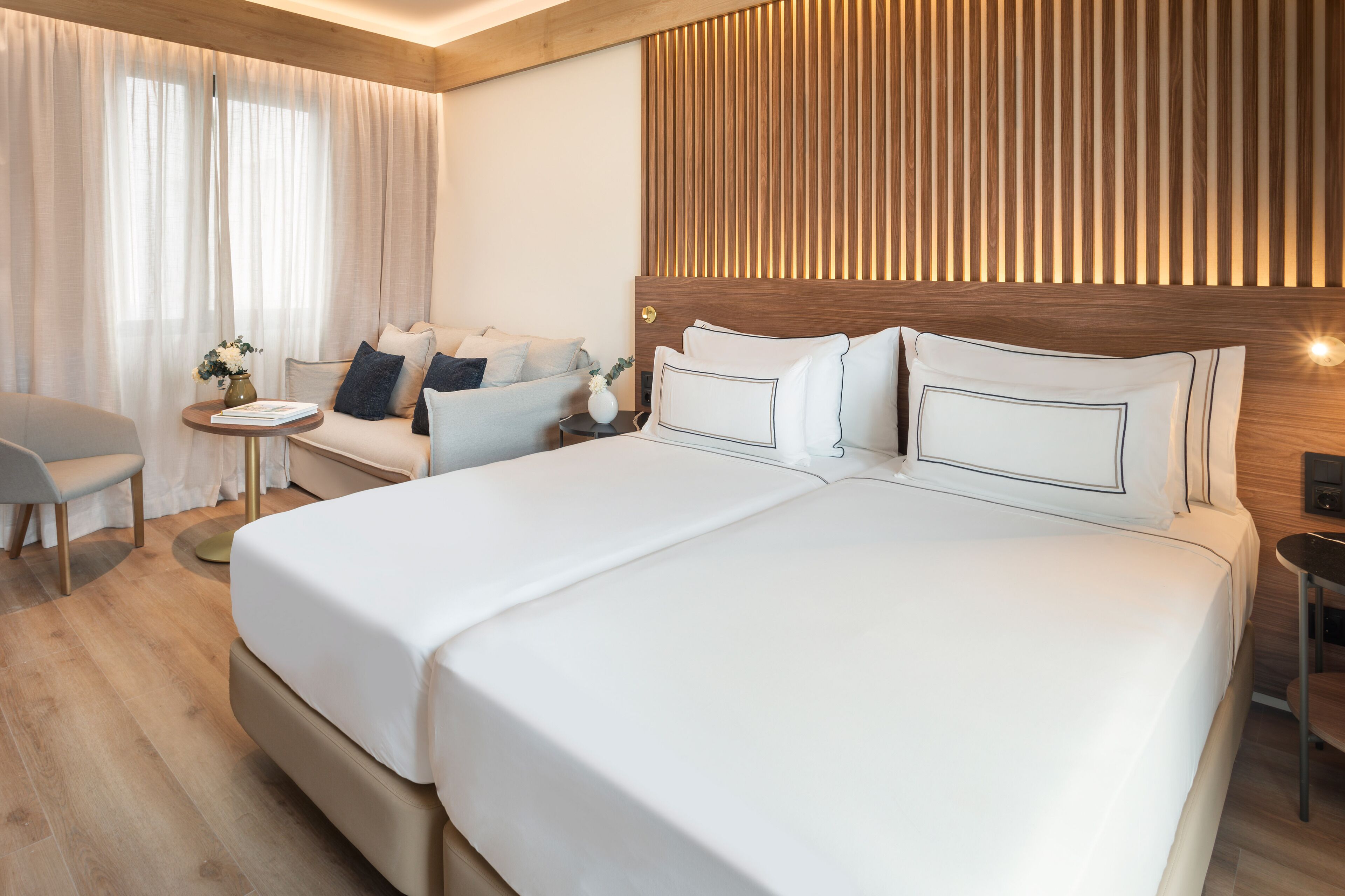 A modern hotel room with a large bed, a sofa, a small table, and a chair.