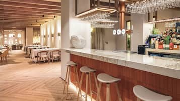 Un espace bar moderne doté d’un comptoir en marbre, de tabourets et d’une variété de bouteilles et de verres.