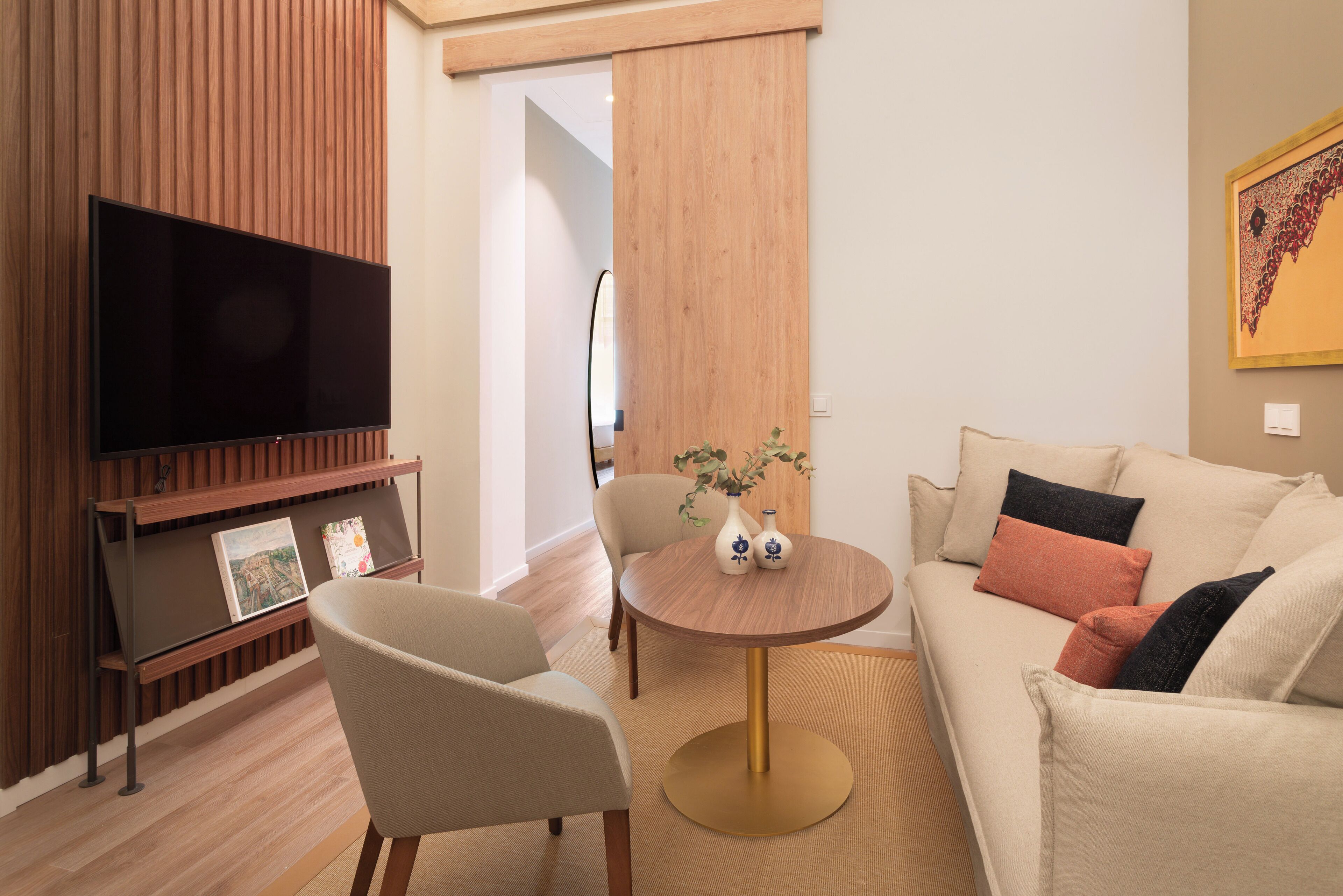 A modern living room with a flat-screen TV, a round wooden coffee table, a beige sofa, and a chair.