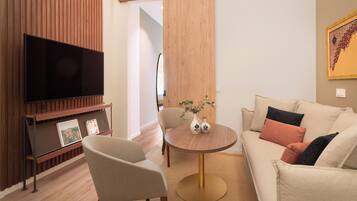 A modern living room with a flat-screen TV, a round wooden coffee table, a beige sofa, and a chair.