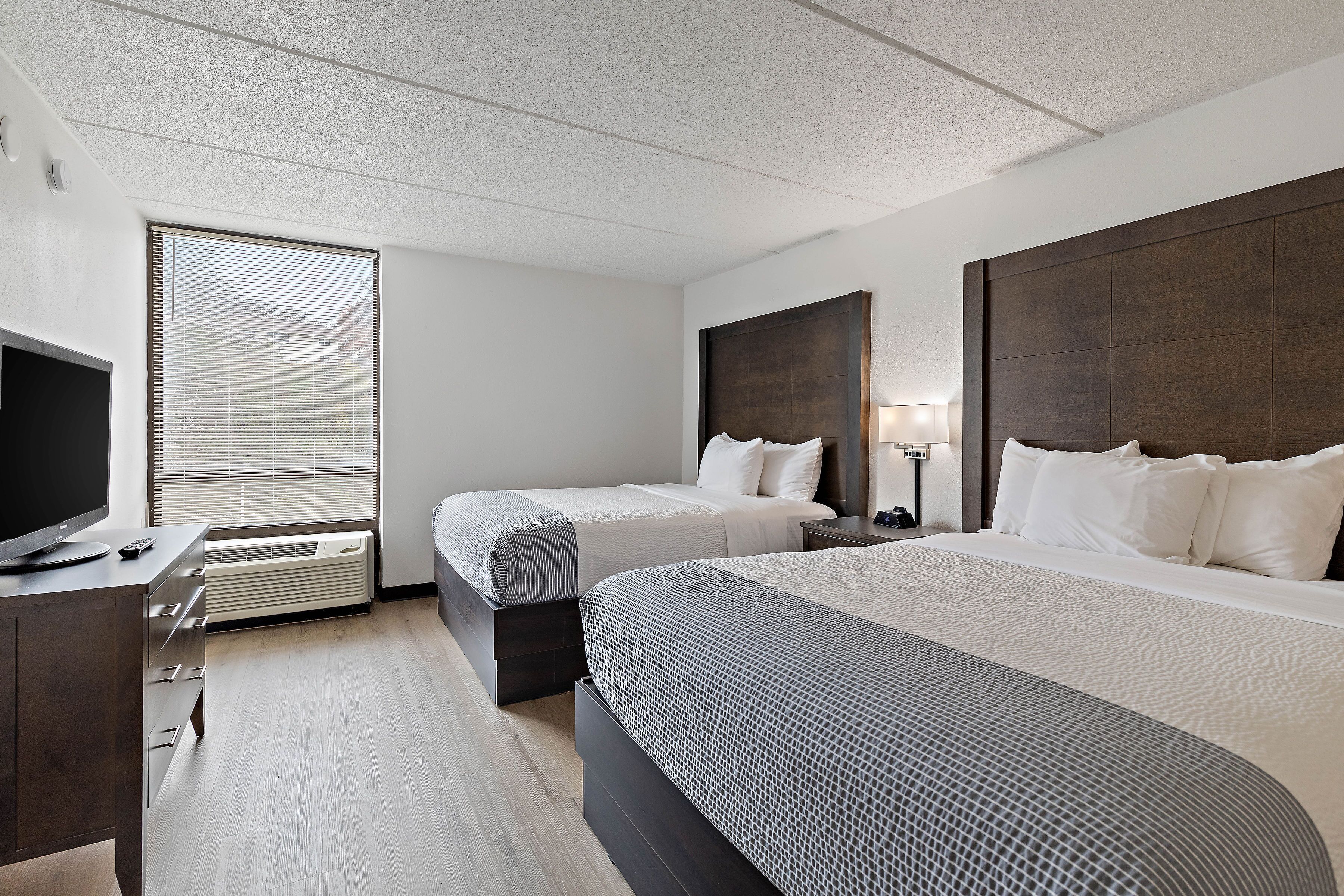Habitación de hotel con dos camas, un escritorio con televisor y una ventana con persianas.