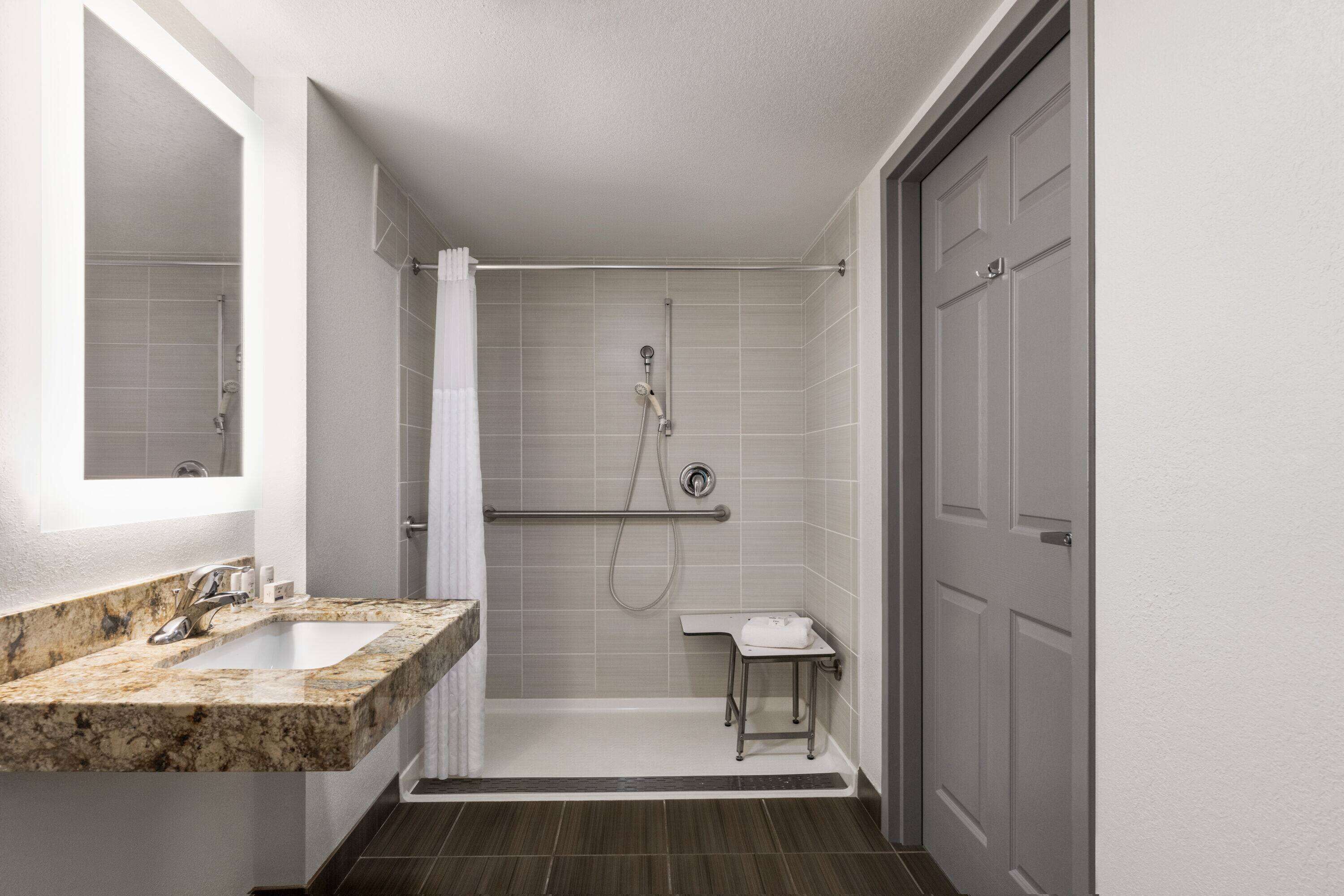 A modern bathroom with a marble sink, a glass shower enclosure, and a small vanity table.