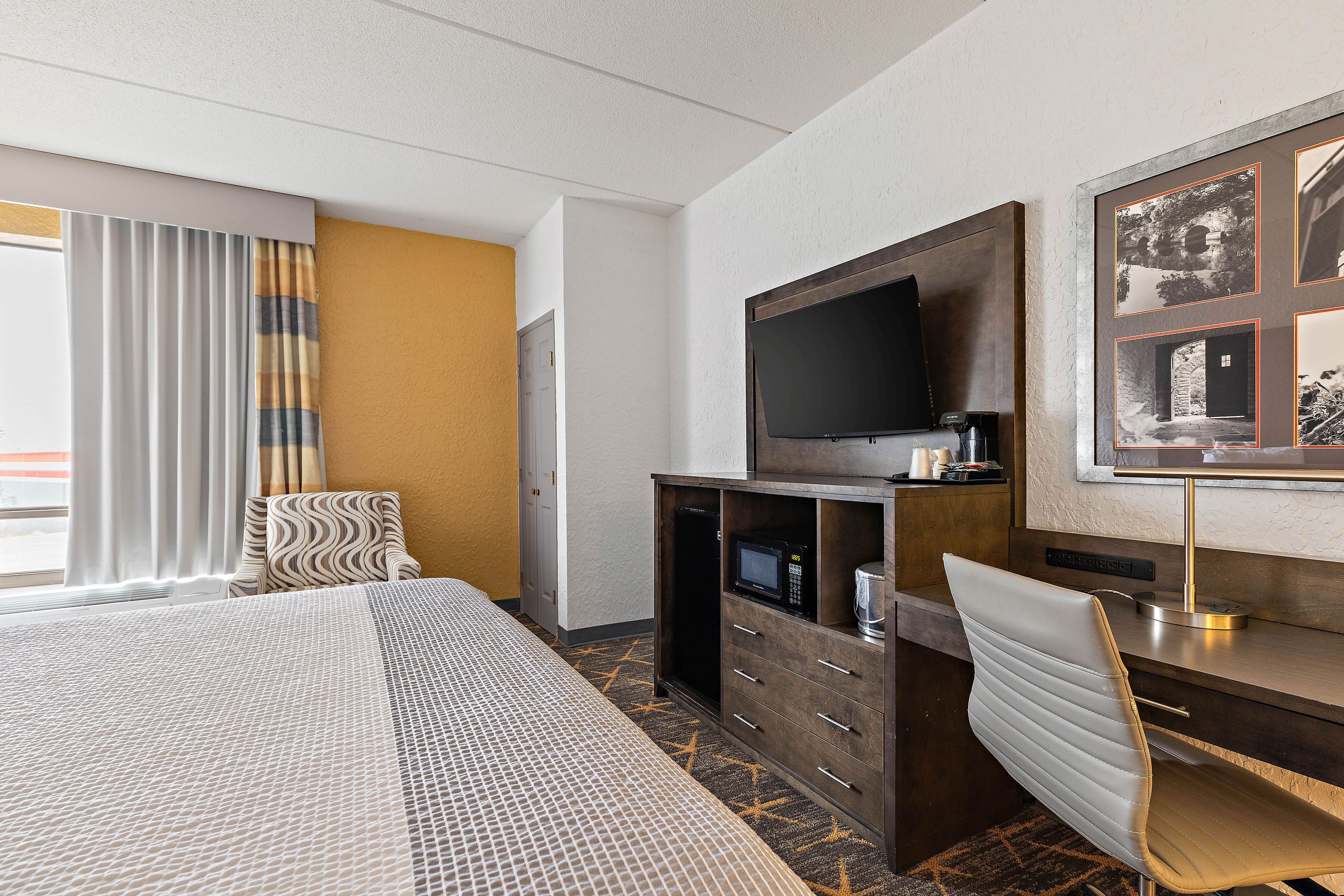 Une chambre d’hôtel avec un grand lit, un bureau doté d’une télévision à écran plat, un four à micro-ondes et une chaise.