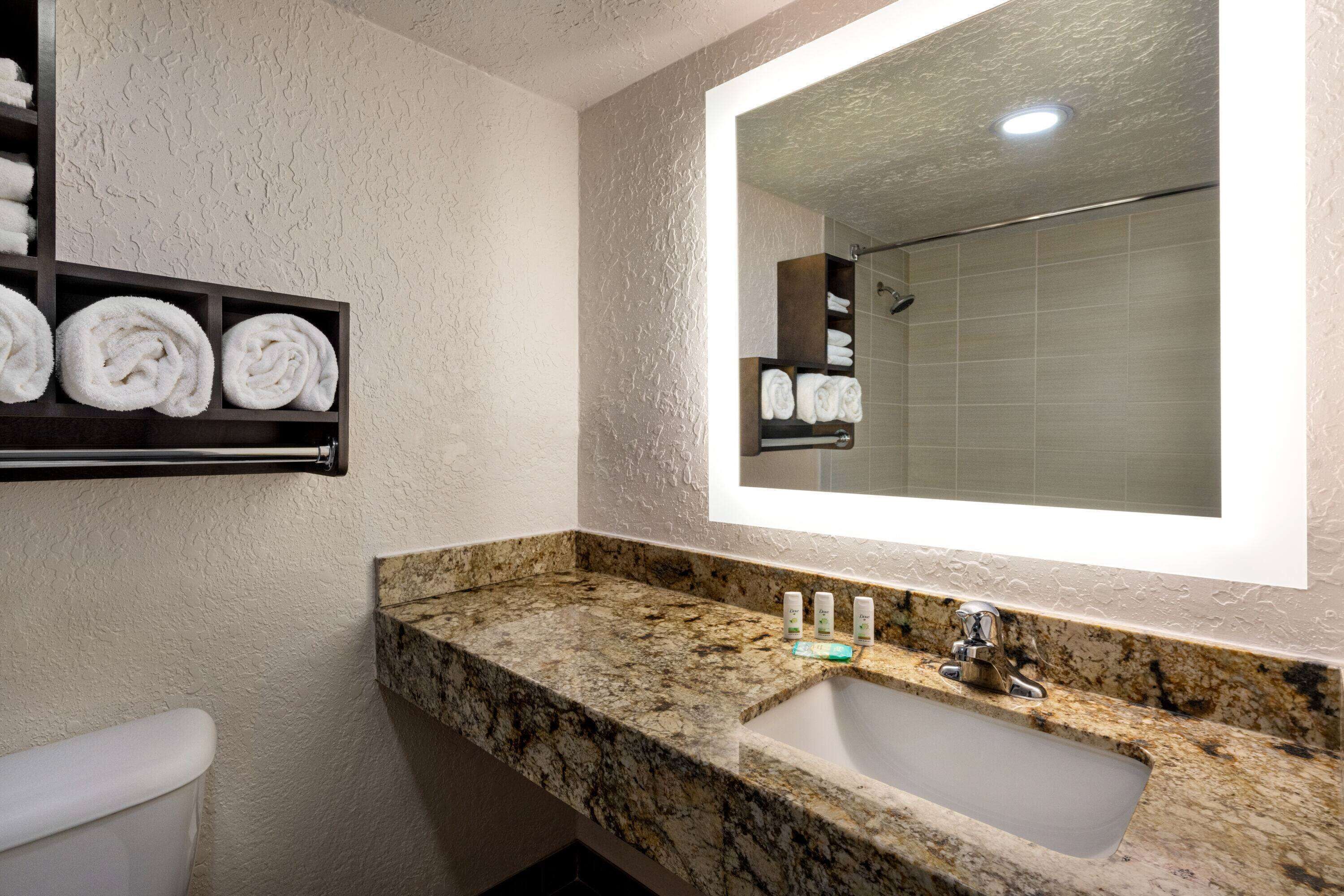 A bathroom with a marble countertop, a sink, and a mirror. There are towels on a shelf above the sink.