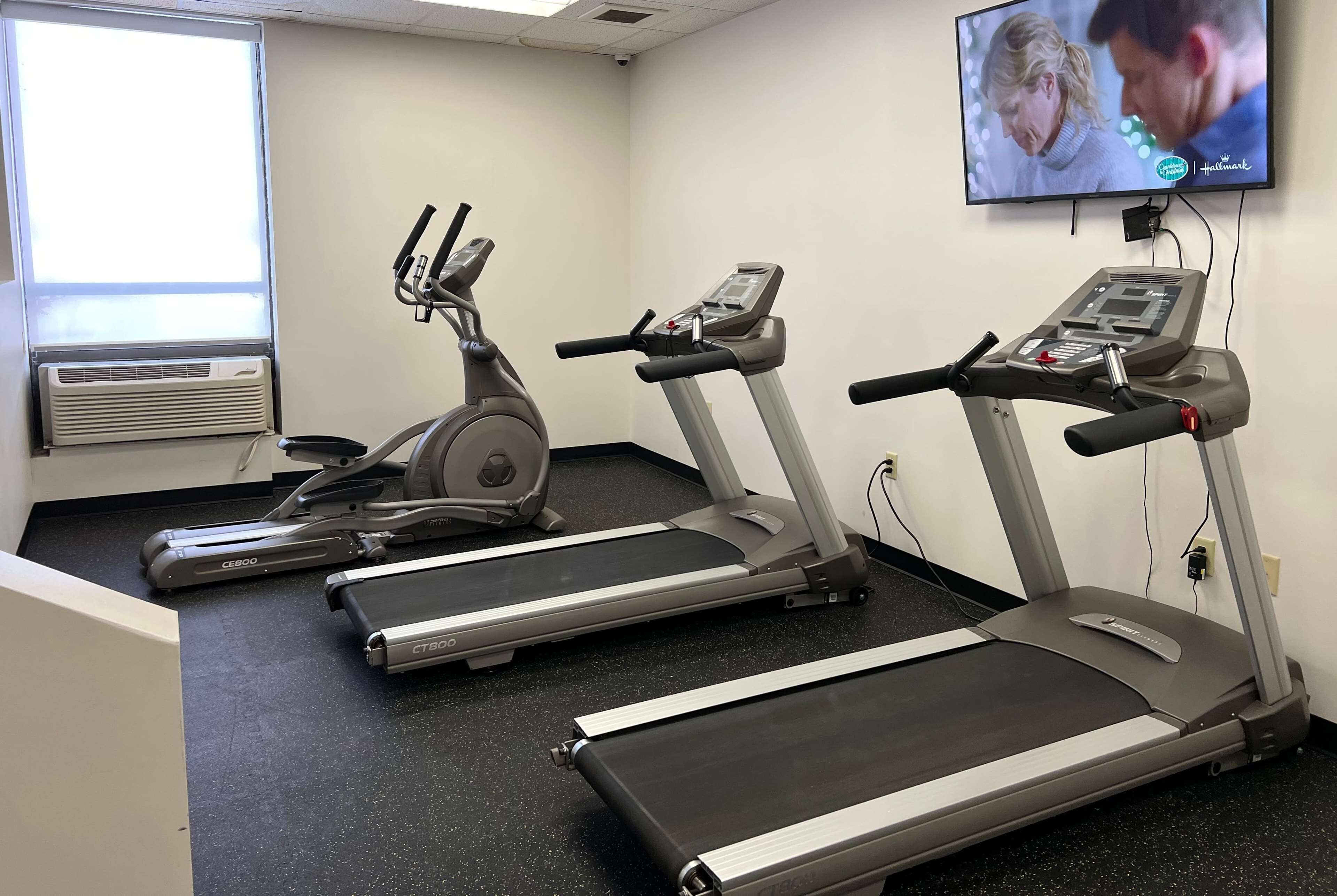 Un gimnasio con cintas de correr, una bicicleta estática y una pantalla de televisión mostrando un programa.