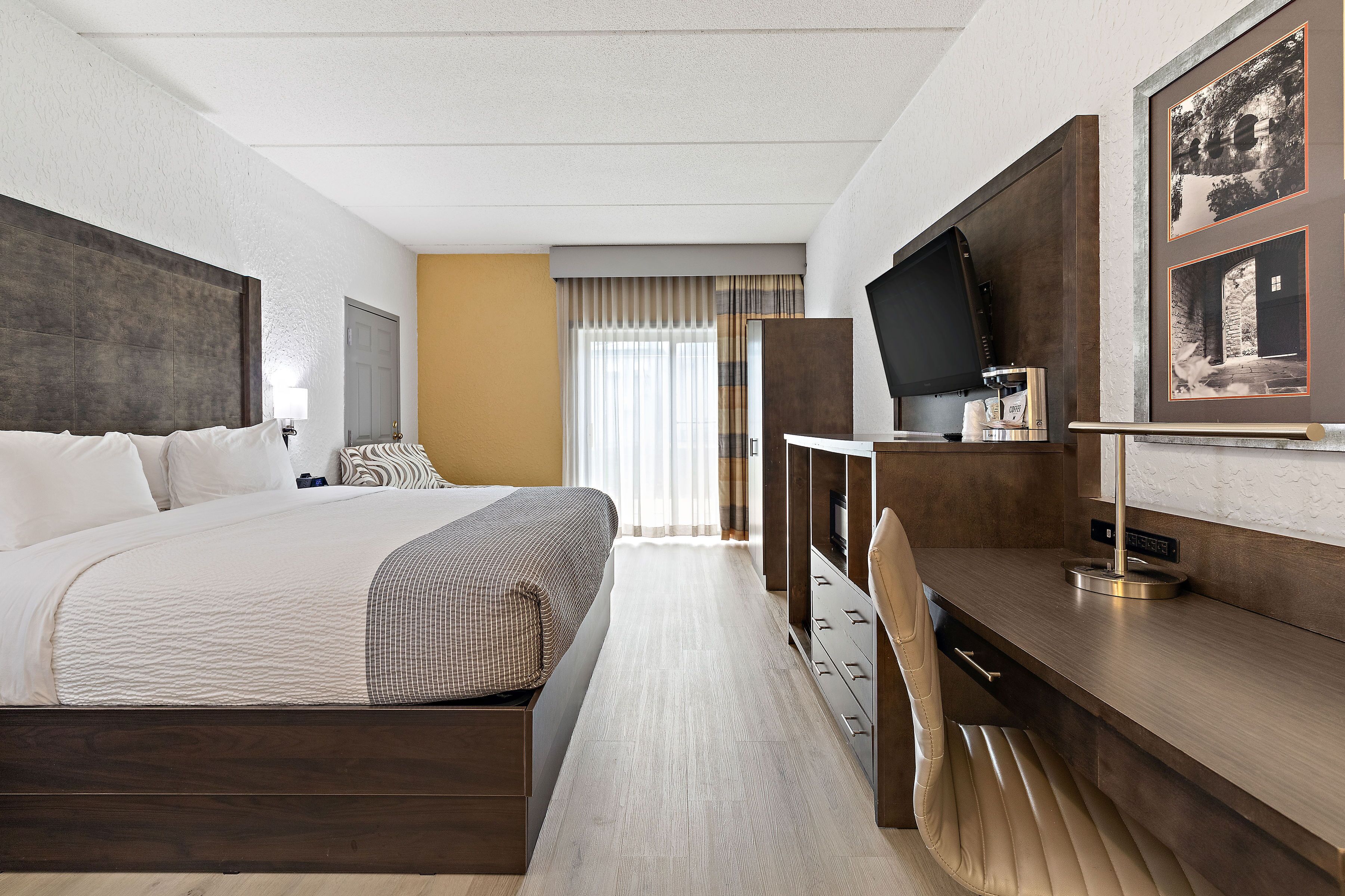 Een hotelkamer met een groot bed, een bureau met een koffiezetapparaat, een televisie en een lijst aan de muur.