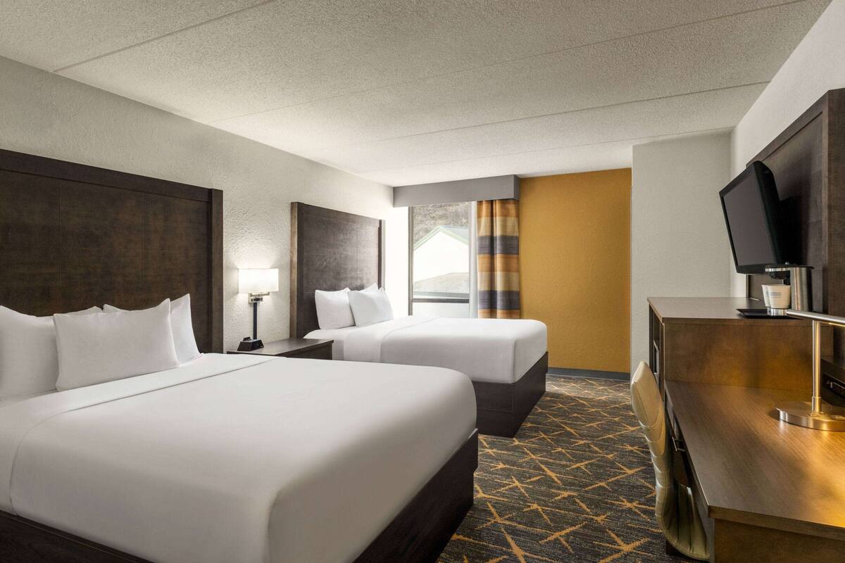 A hotel room with two beds, a desk, a television, and a window with curtains.