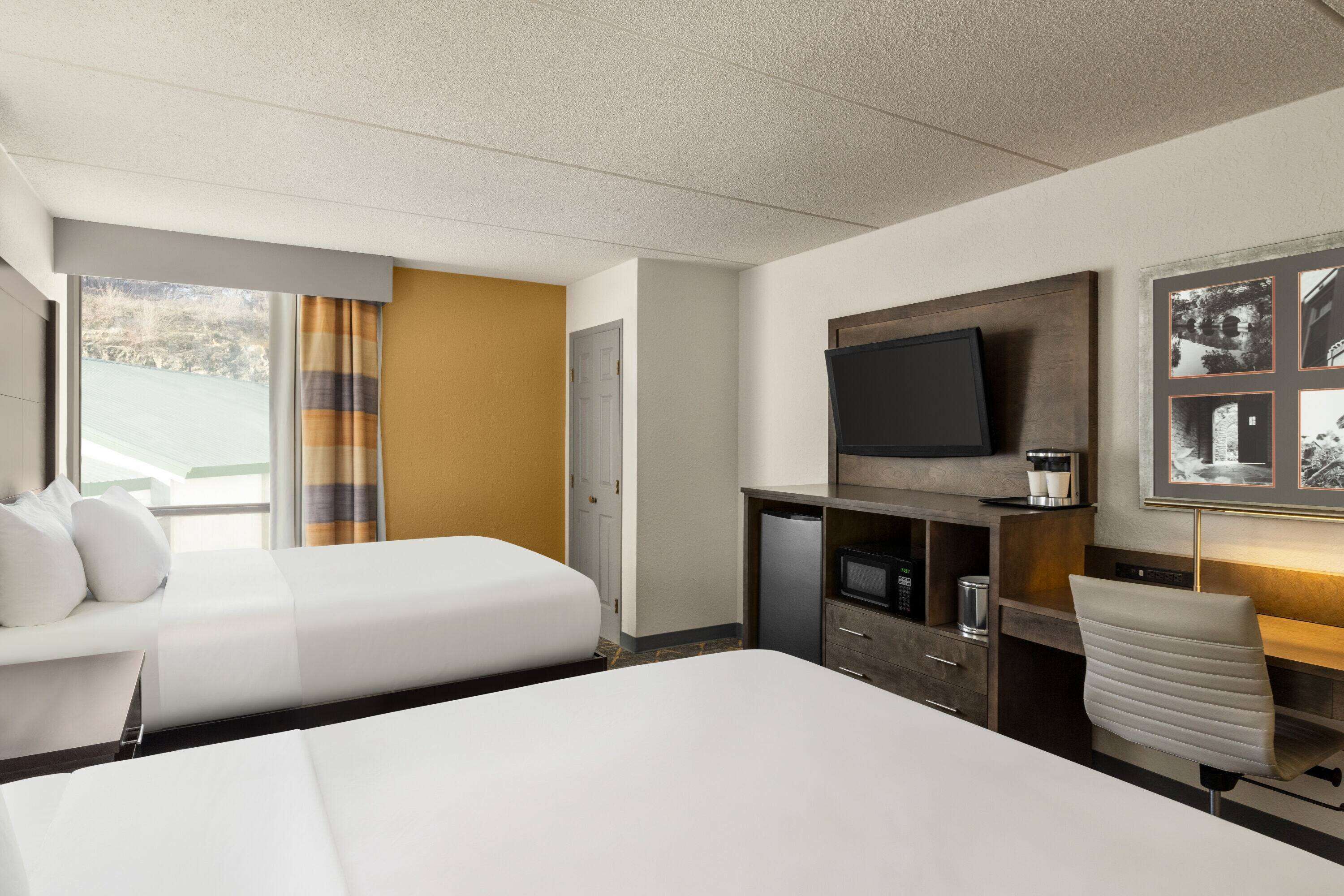 Une chambre d’hôtel avec deux lits, une télévision, un bureau et une fenêtre avec des rideaux.