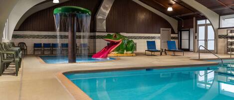 Una piscina interior con tobogán, zona de estar y una gran estatua de rana.