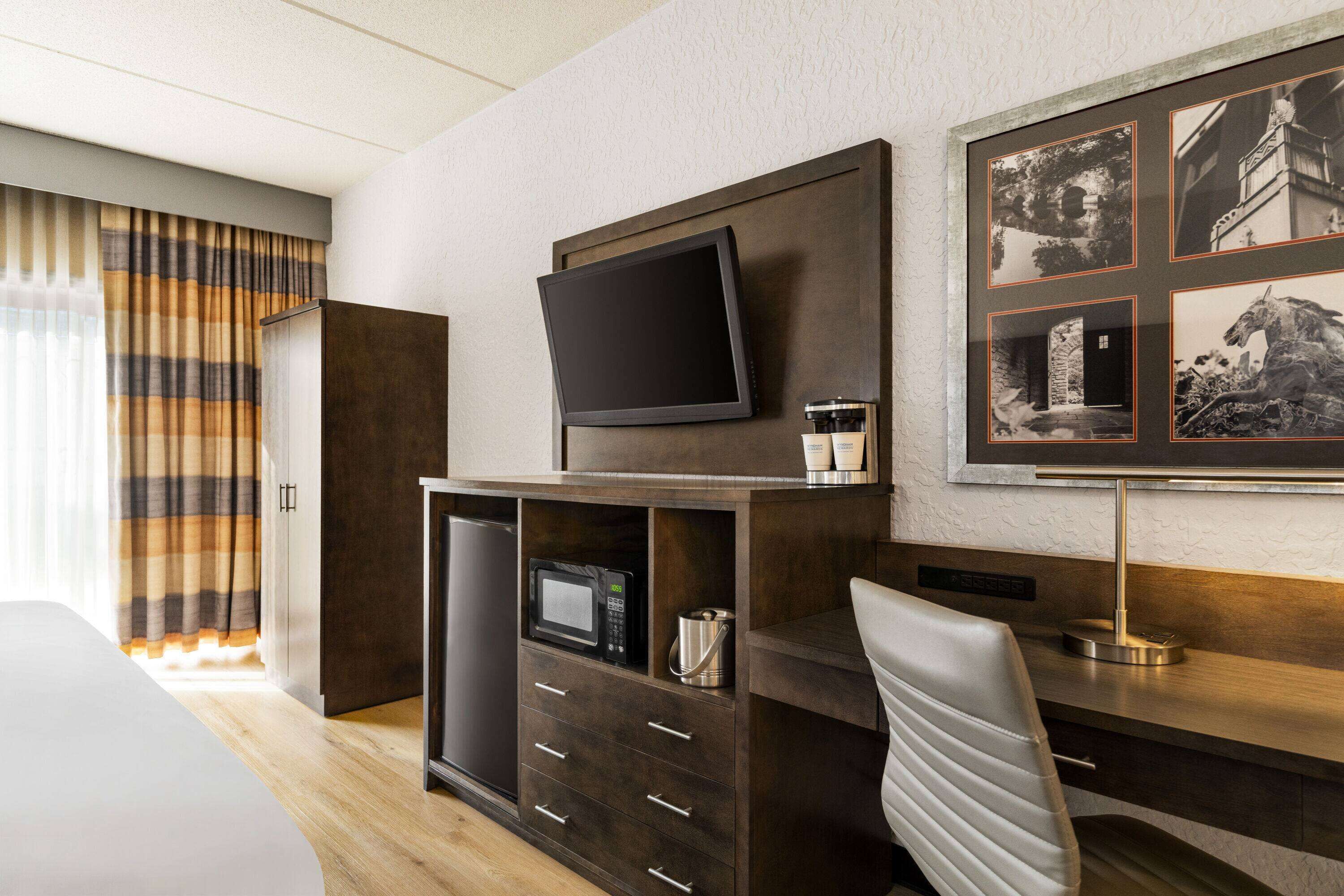 A hotel room with a bed, a desk with a flat-screen TV, a coffee machine, a microwave, and a framed picture on the wall.