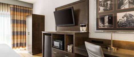 A hotel room with a bed, a desk with a flat-screen TV, a coffee machine, a microwave, and a framed picture on the wall.