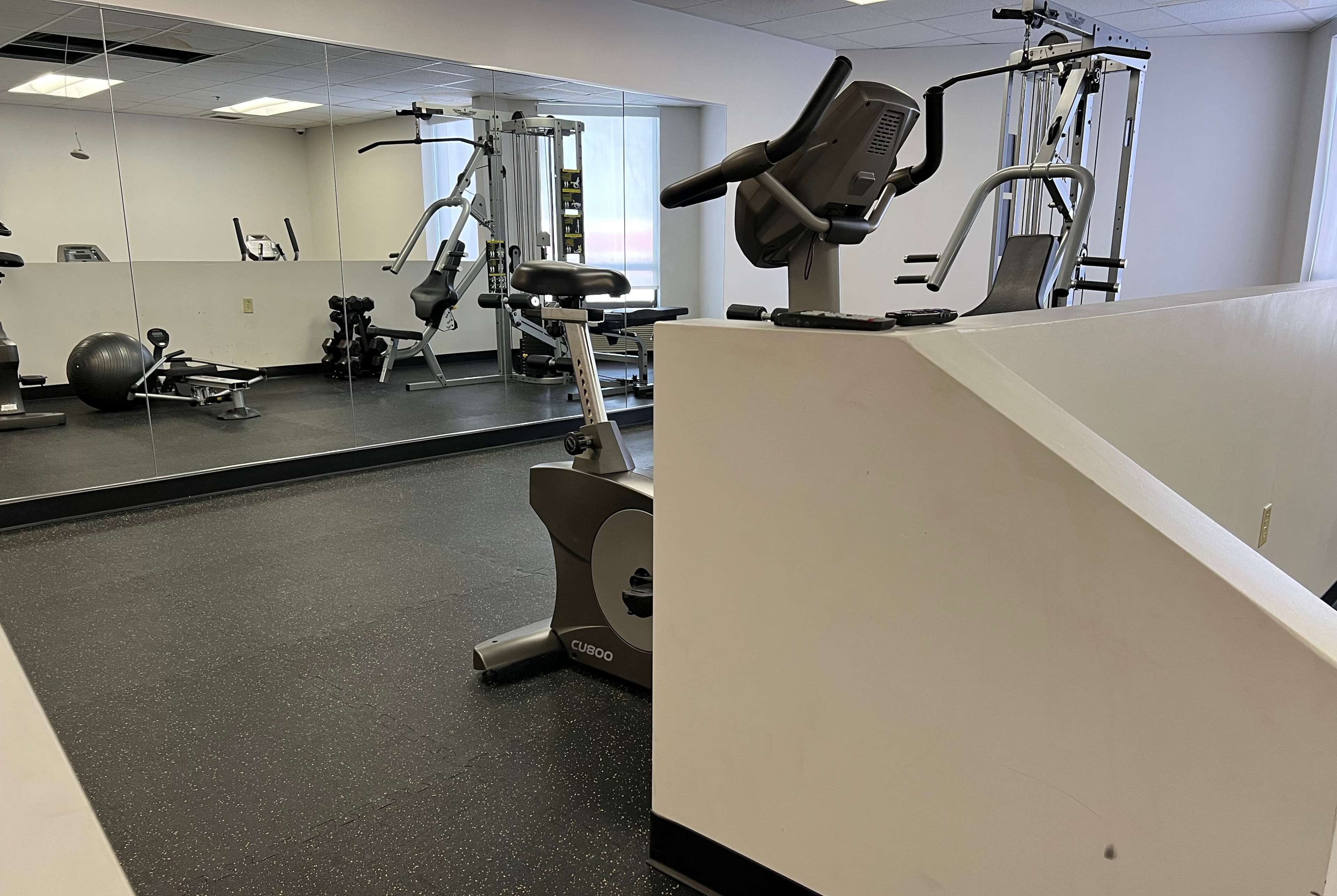 A gym with exercise equipment, a mirrored wall, and a black speckled floor.