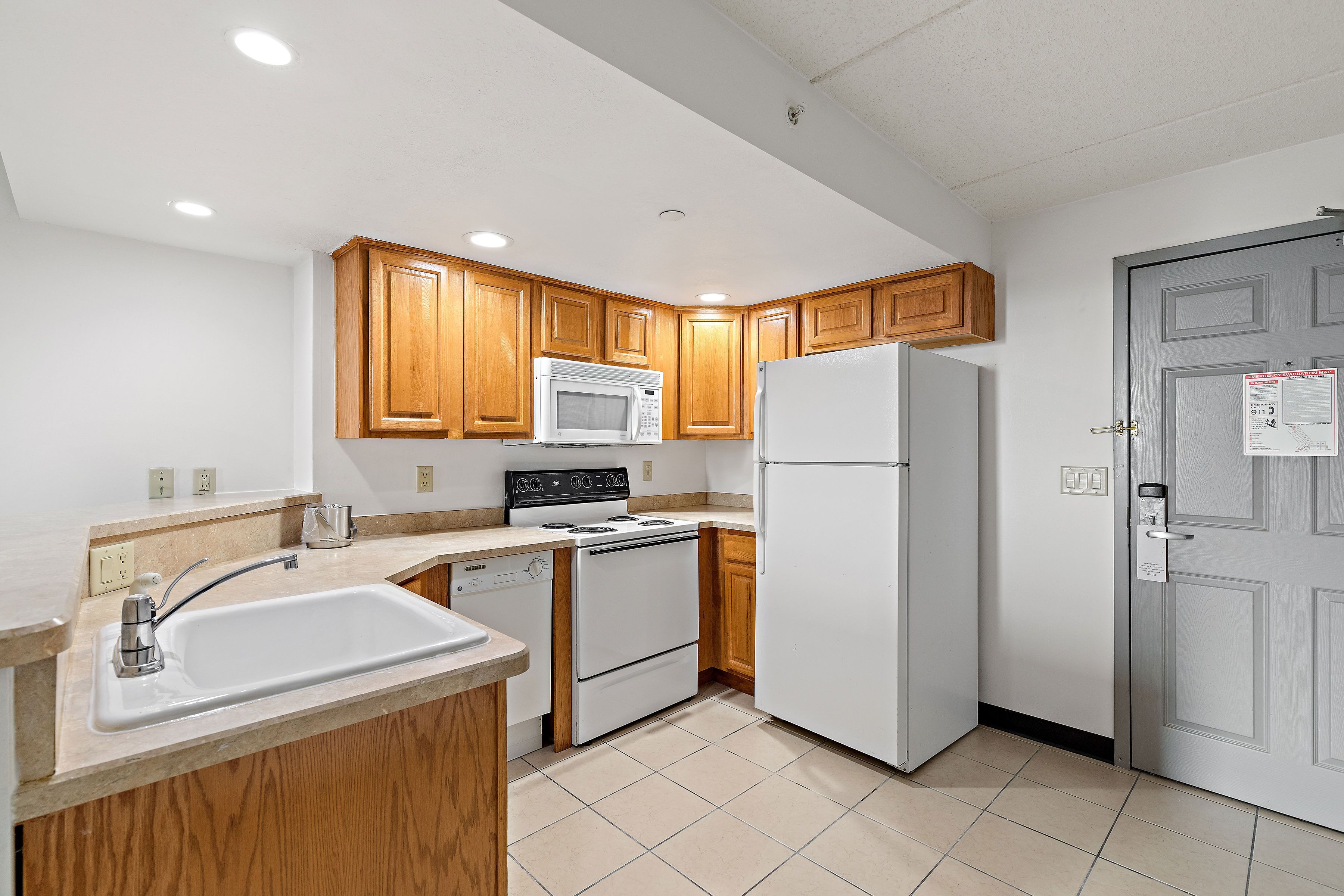 A kitchen with wooden cabinets, a white microwave, a stove, a sink, and a refrigerator.