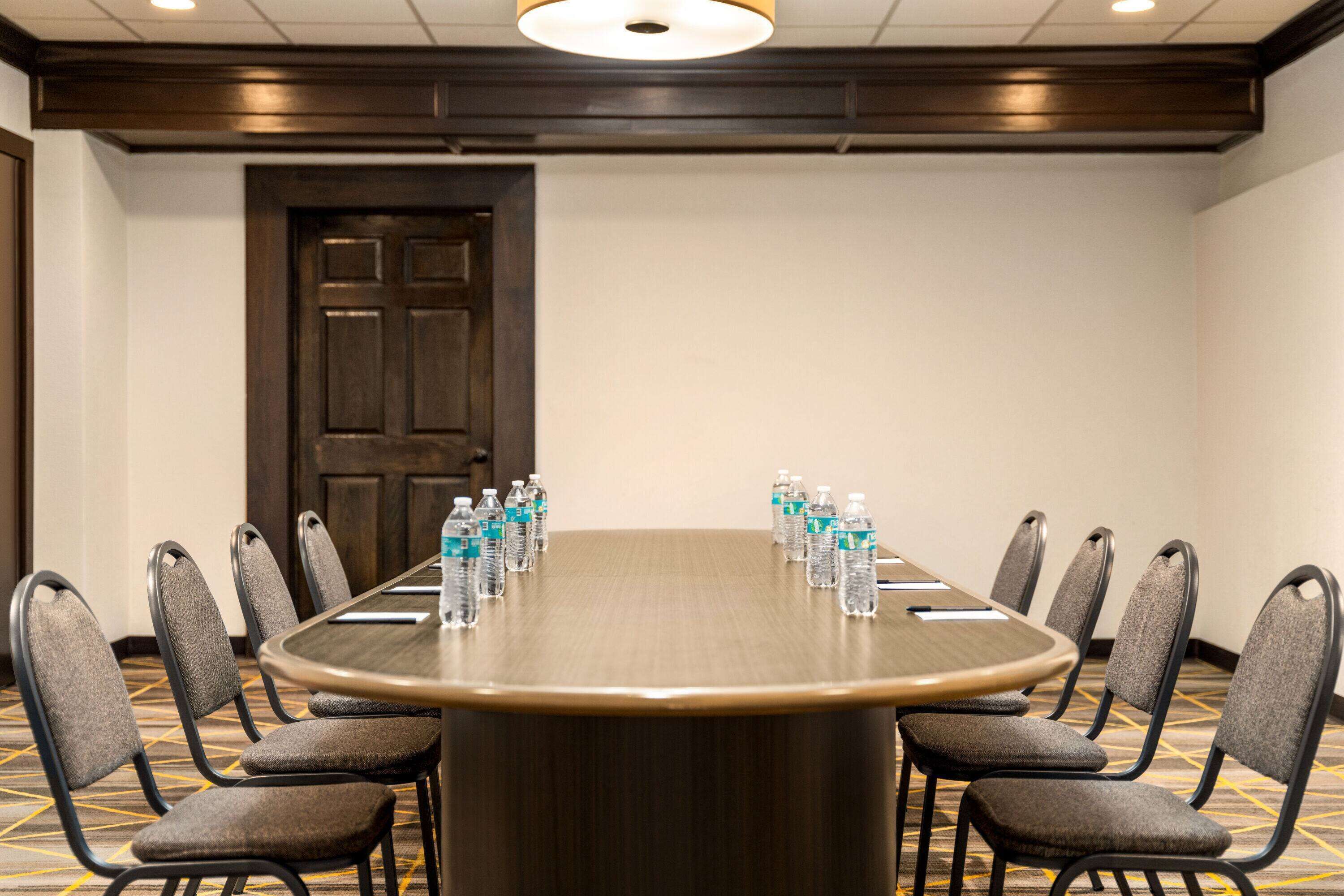 A conference room with a large round table, eight chairs, and water bottles on the table.
