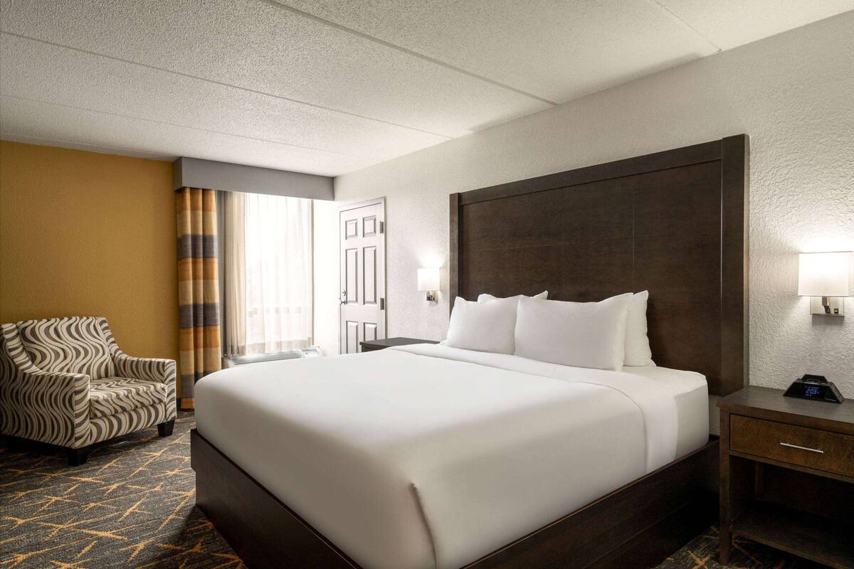 A hotel room with a large bed, a chair, a nightstand, and a lamp.