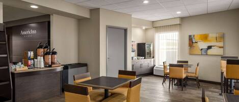 A hotel lobby with a coffee station, seating area, and a painting on the wall.