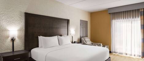 A hotel room with a large bed, a nightstand, a chair, and a window with curtains.