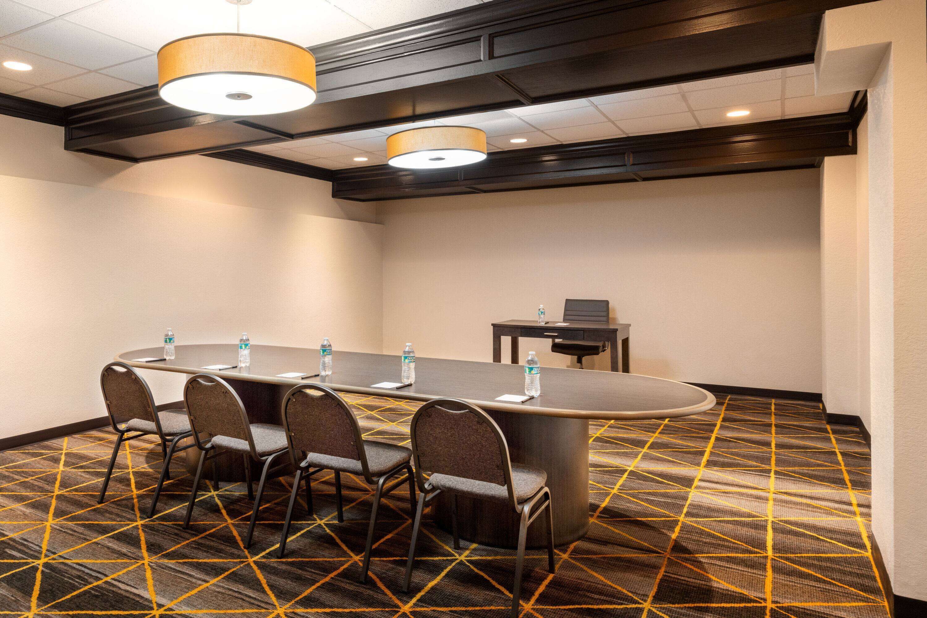 A conference room with a long table, four chairs, two water bottles, and a small table with a chair.