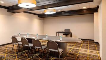 A conference room with a long table, four chairs, two water bottles, and a small table with a chair.