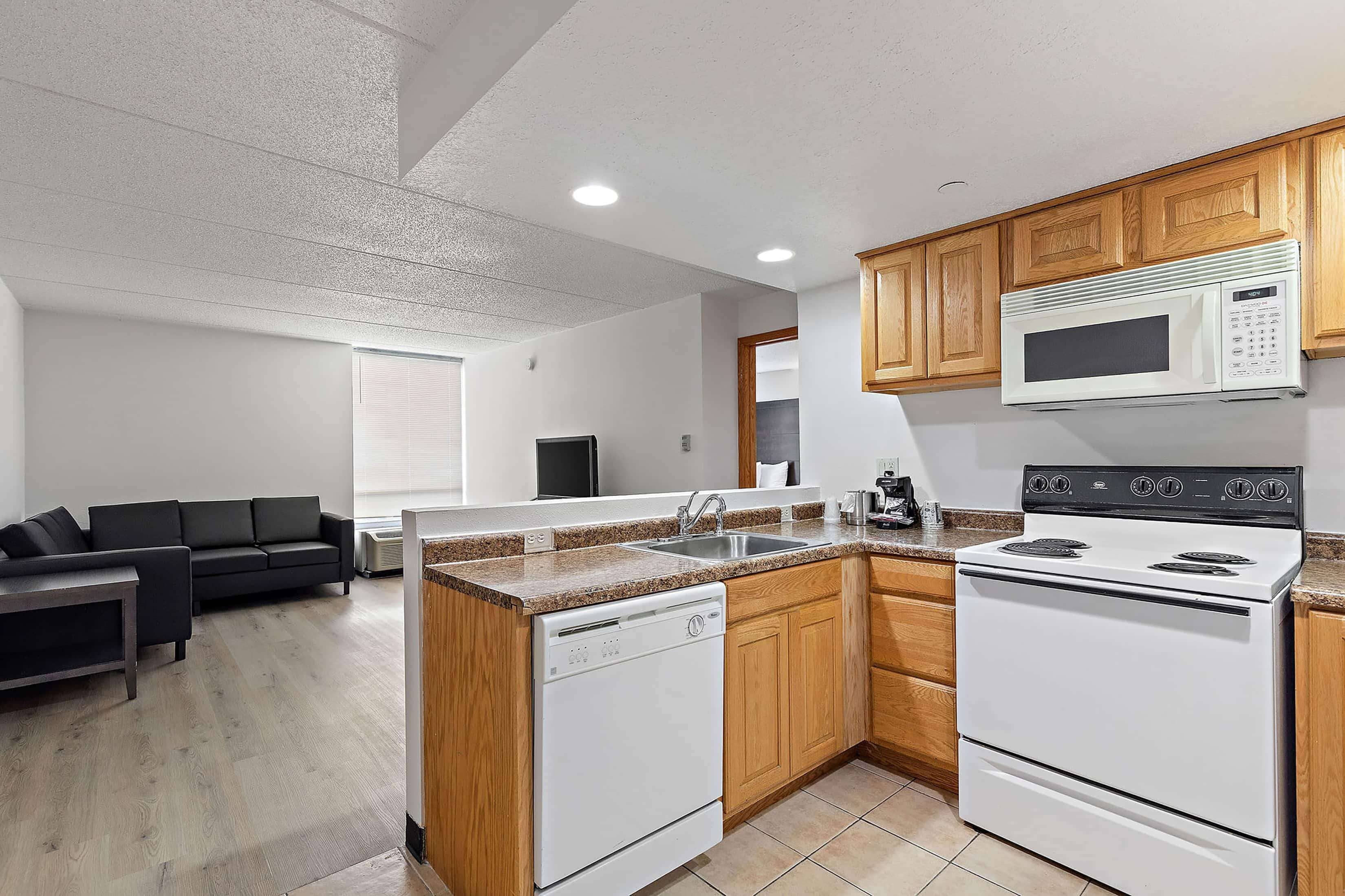 A compact kitchen with a dishwasher, stove, microwave, and wooden cabinets.