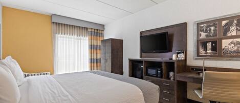 A hotel room with a large bed, a desk with a chair, a flat-screen TV, and a wall-mounted TV.