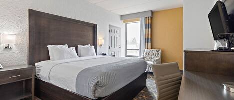 A hotel room with a large bed, a desk with a computer, a chair, and a TV.