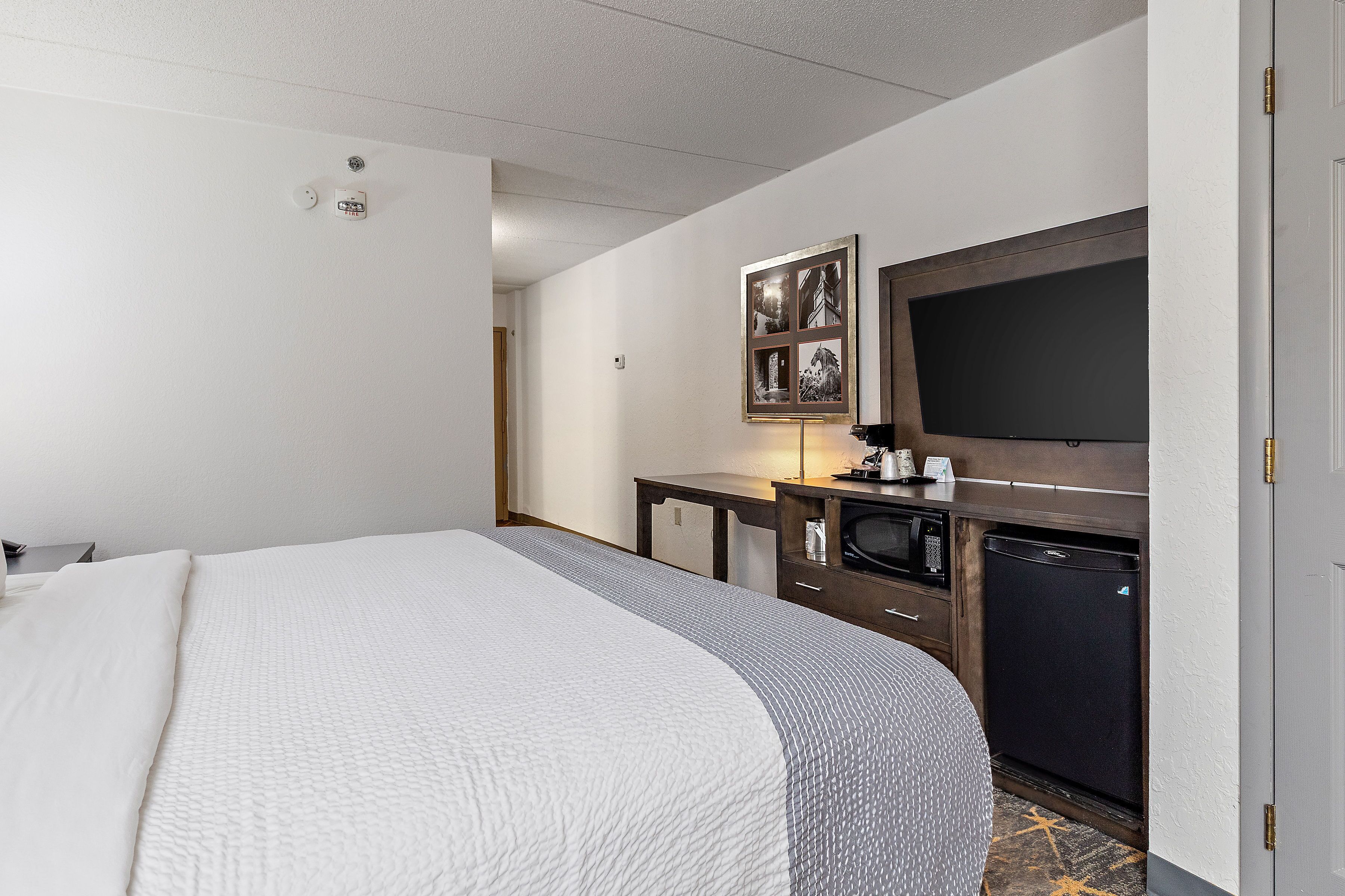 Habitación de hotel con una cama grande, televisión de pantalla plana, escritorio pequeño con lámpara y microondas.