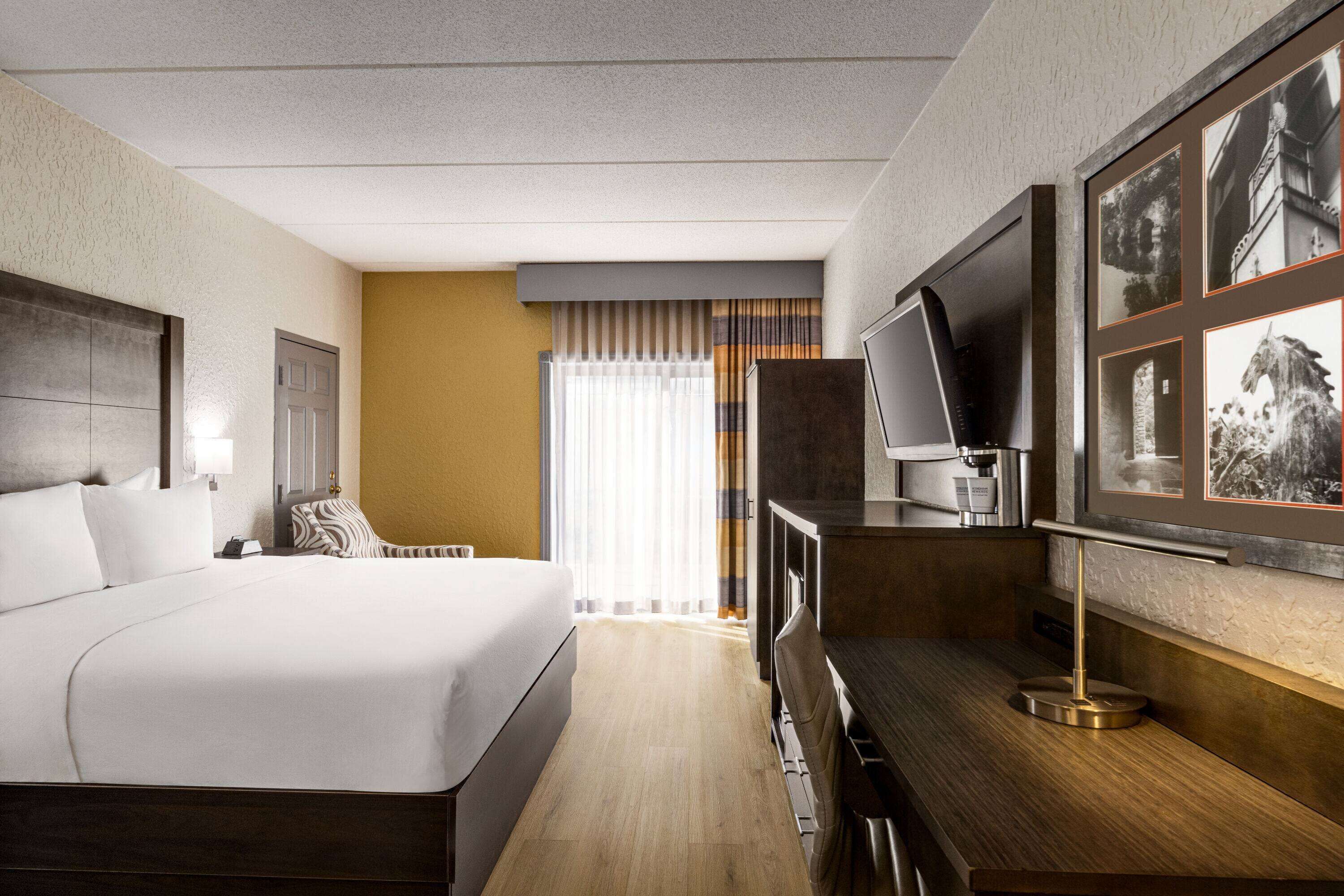 A hotel room with a large bed, a desk with a television, and framed pictures on the wall.