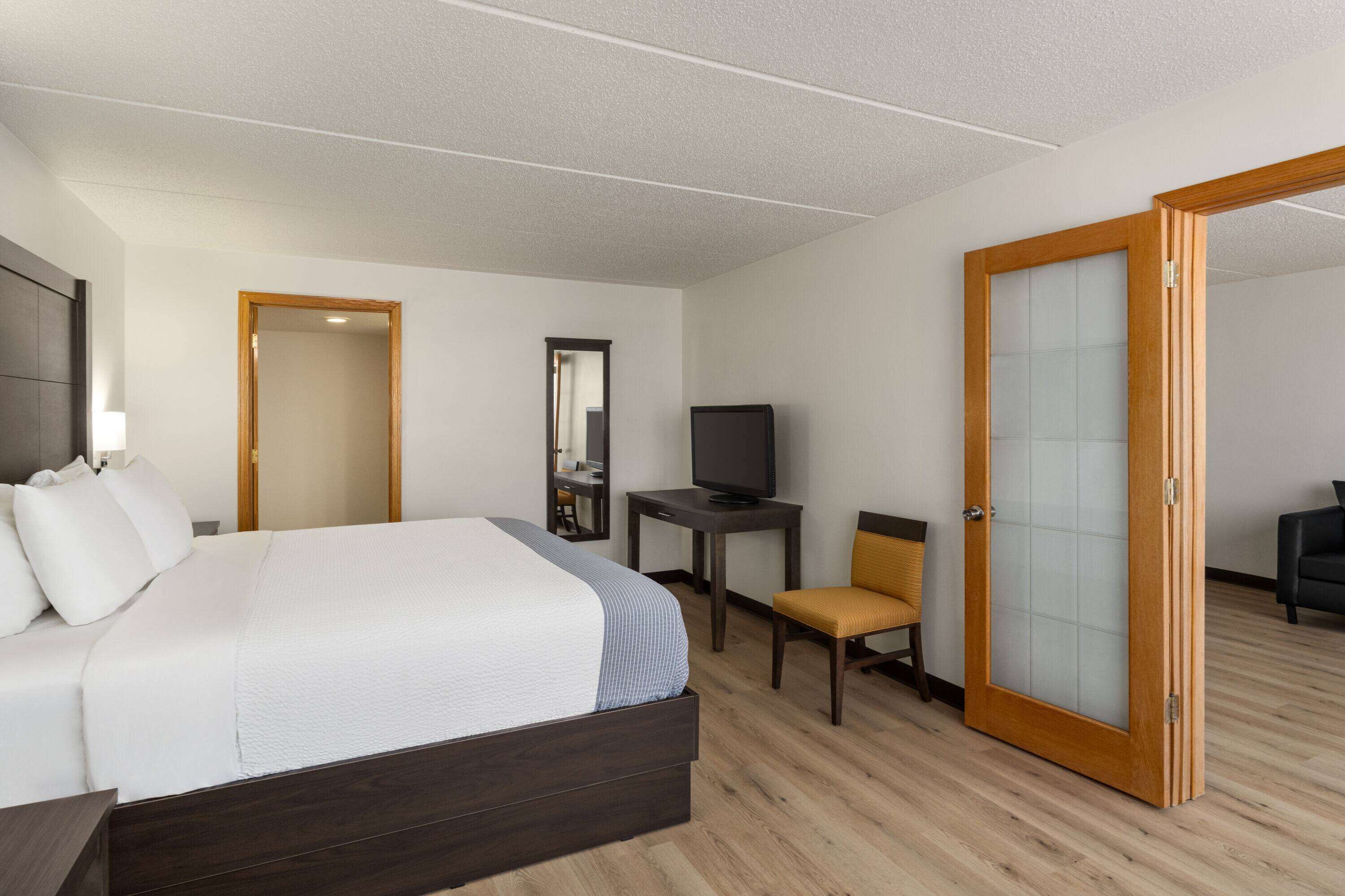 A hotel room with a large bed, a desk with a television, a chair, and a wardrobe.