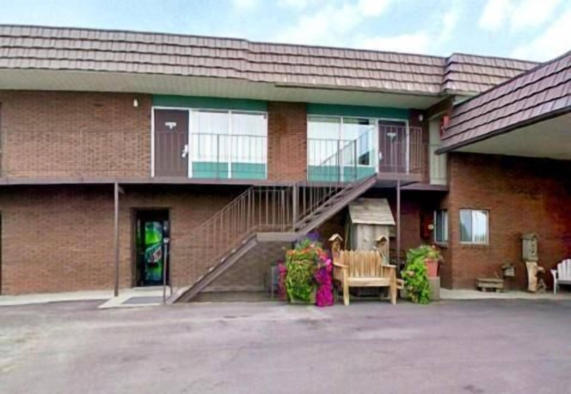 Een gebouw met twee verdiepingen, een bakstenen gevel, een overdekte gang en een klein portaaltje met een bankje.