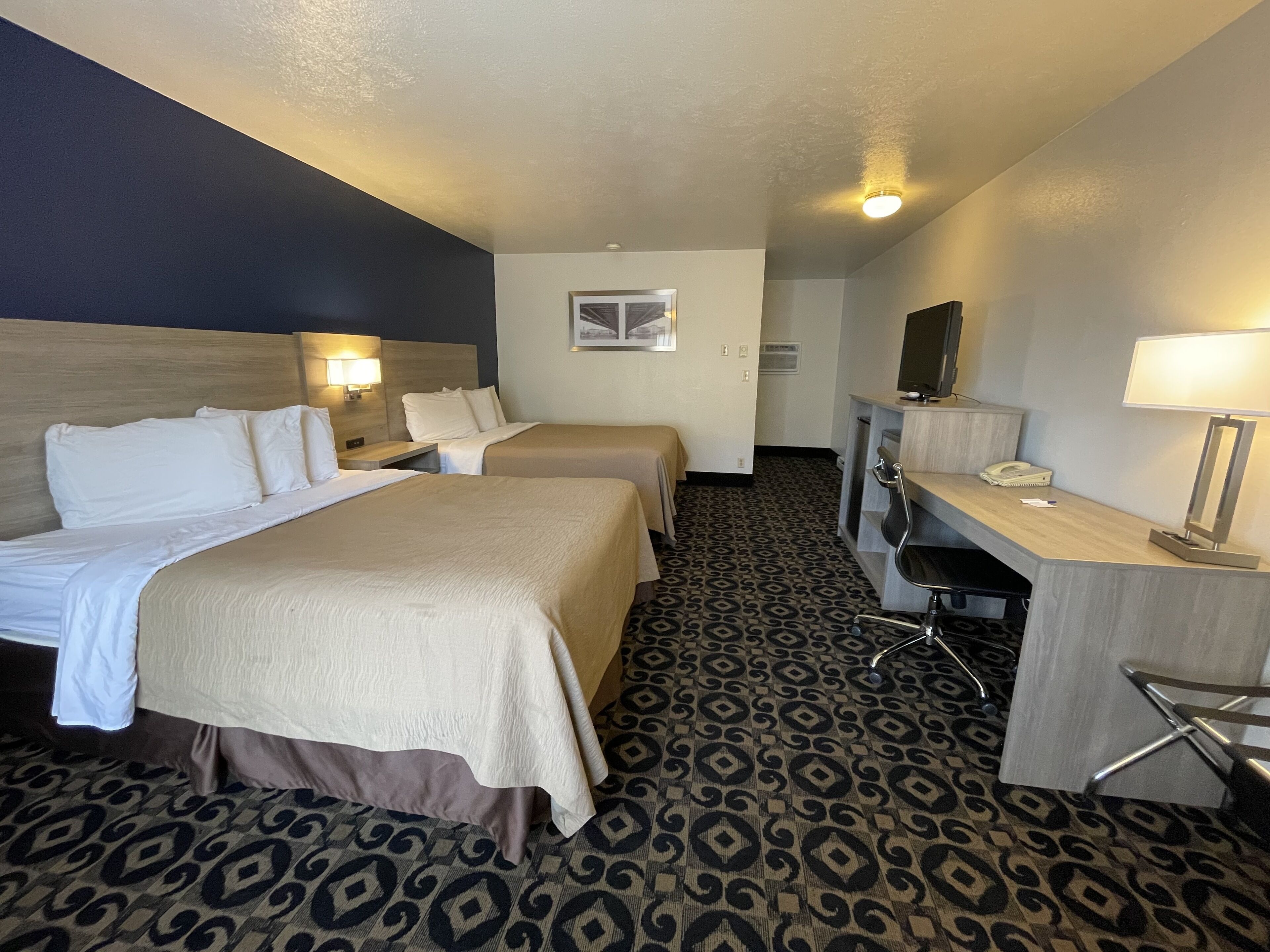 A hotel room with two beds, a desk, a chair, a desk lamp, a telephone, and a television.