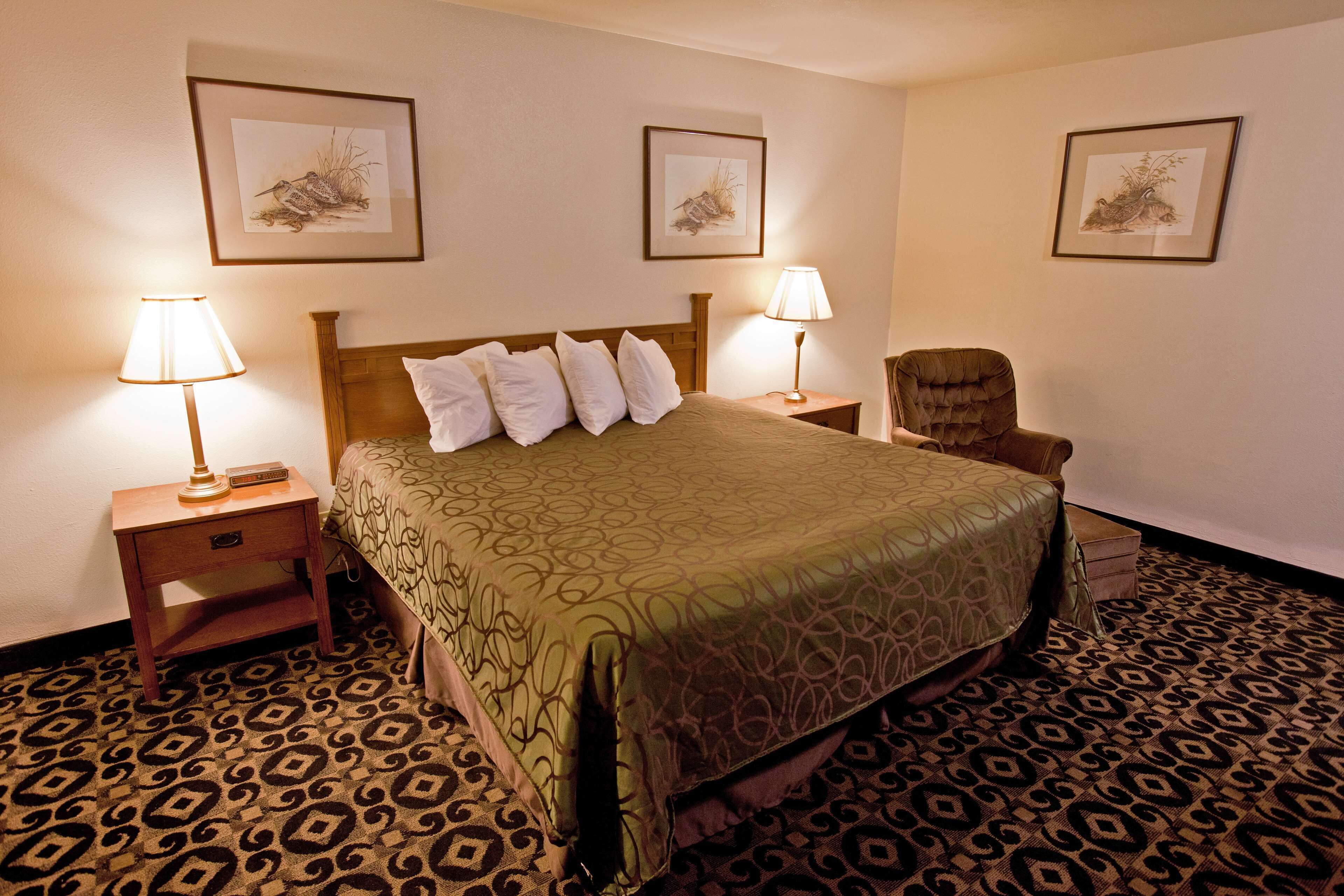 A hotel room with a large bed, two bedside tables with lamps, a chair, and three framed pictures on the walls.