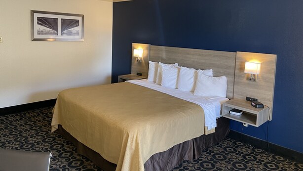A hotel room with a bed, bedside tables, and a wall-mounted picture. - Americas Best Value Inn Roosevelt Ballard (Roosevelt)