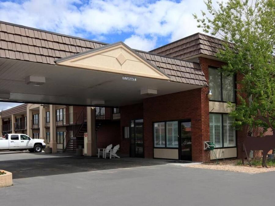 A motel with a covered parking area, brick exterior, and a large tree to the right.