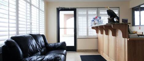 A room with a black leather sofa, a wooden counter with a bird sculpture, and a door leading outside.