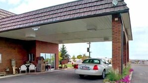 A building with a covered parking area, a brick facade, and a car parked in front. - Americas Best Value Inn Roosevelt Ballard (Roosevelt)