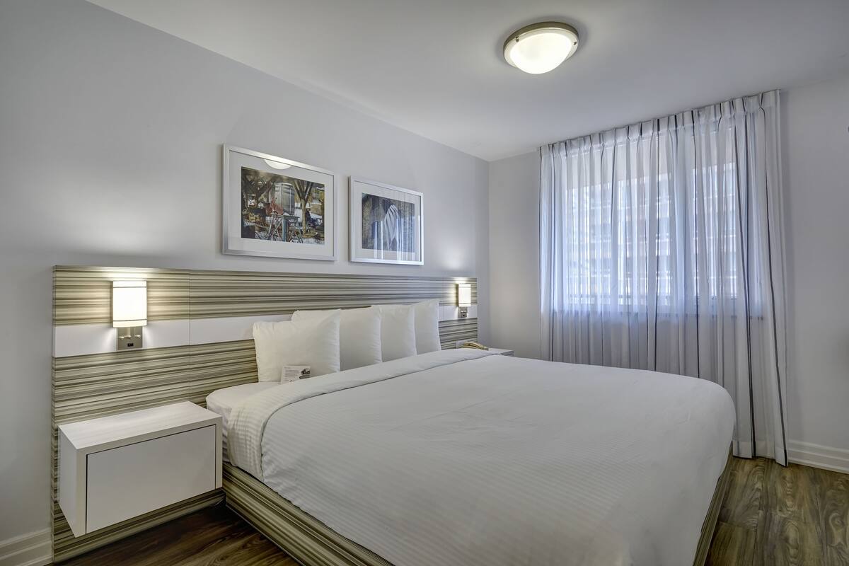A neatly arranged hotel room with a large bed, two bedside tables, a headboard with a light fixture, and two framed pictures on the wall.